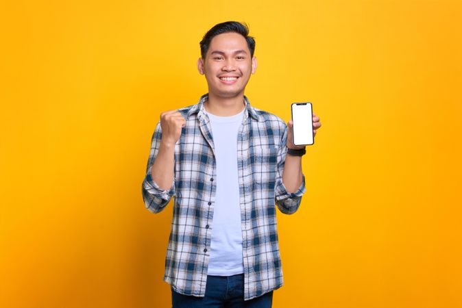 Happy Asian male receiving good news from blank screen of smart phone in studio shoot