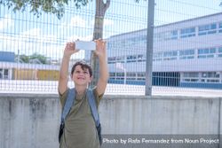 Smiling teenage boy taking selfie in front of school fence 5pmMO4