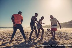 Group of friends playing soccer together on sandy beach in the afternoon bYPp64
