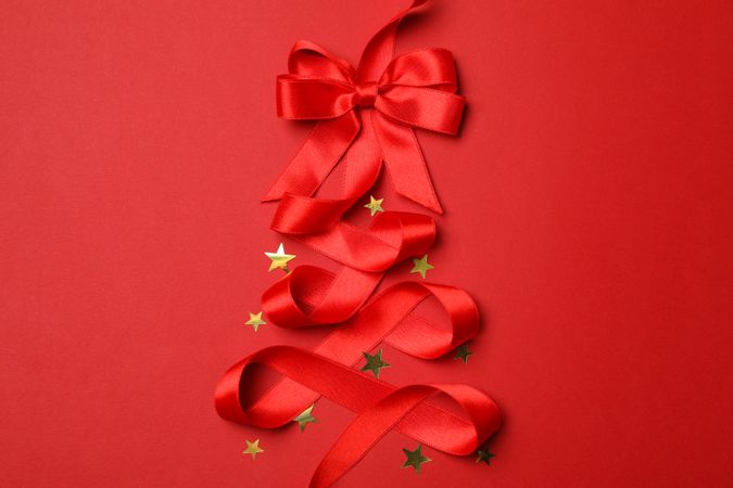 Red ribbon and glitter stars on red background, space for text