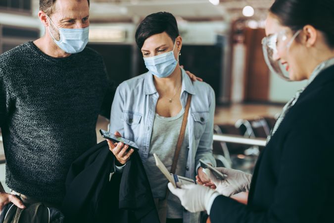 Tourist couple in face masks at check-in counter with airport staff
