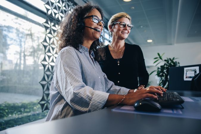 Smiling woman wearing headset working on computer with manager standing by