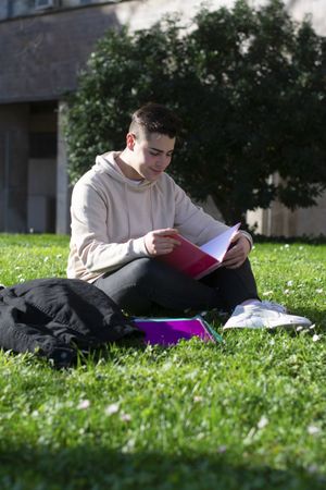 Young student sitting in park studying with his notes
