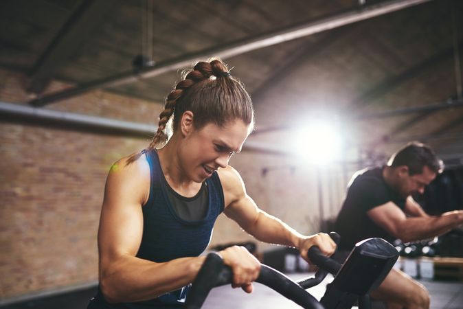 Strong woman exercising beside male on exercise fan bike