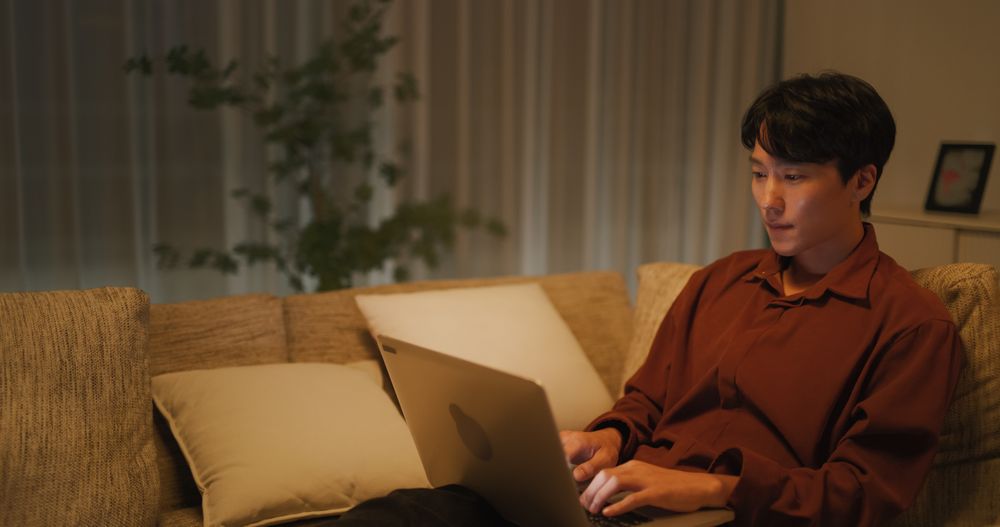 Young Asian Male Browsing Internet in The Evening in His Apartment