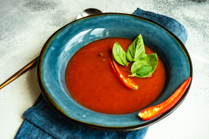 Spanish soup of tomato gazpacho with basil and pepper garnish in blue bowl