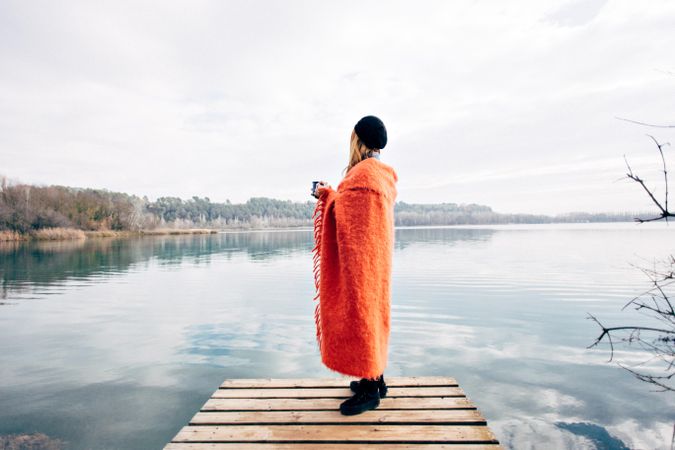 Woman wrapped in warm blanket standing on pier