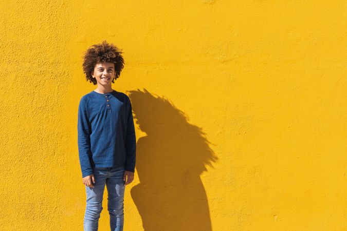 Black boy with curly hair standing on yellow wall