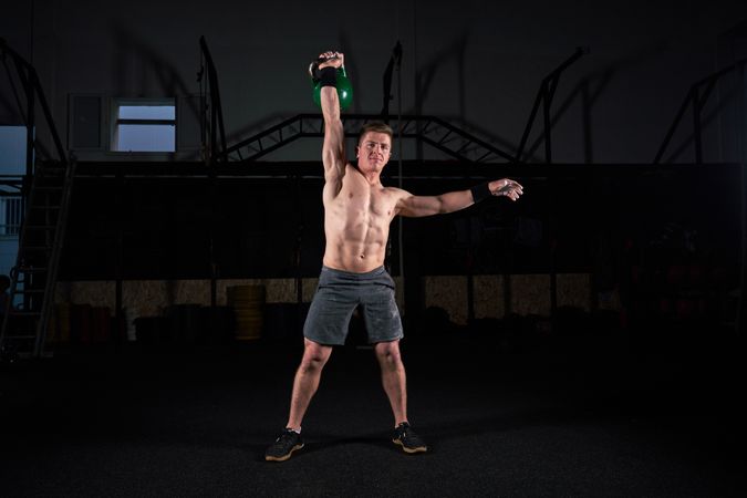 Strong shirtless man lifting kettlebell in gym