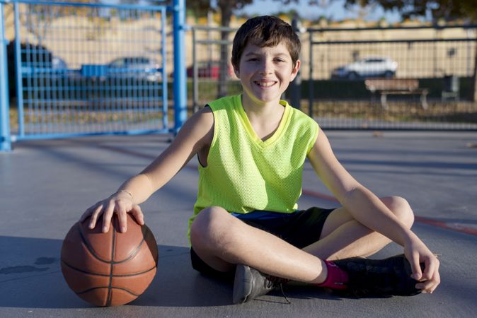 Young smiling basketball player sitting on the court