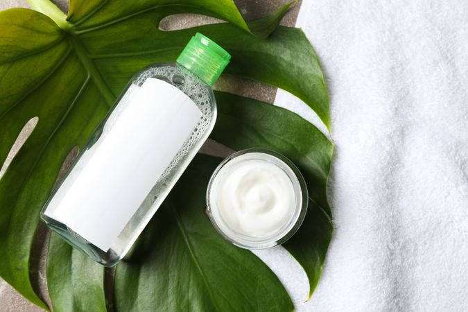 Palm leaf, cream, soap and shampoo on grey background, top view