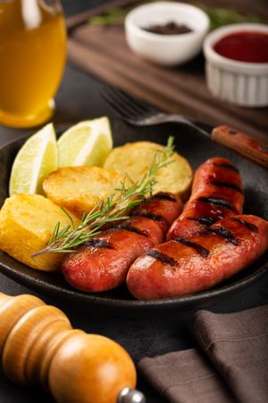 Plate with grilled sausages, potatoes, lime slices and sprig of rosemary, vertical