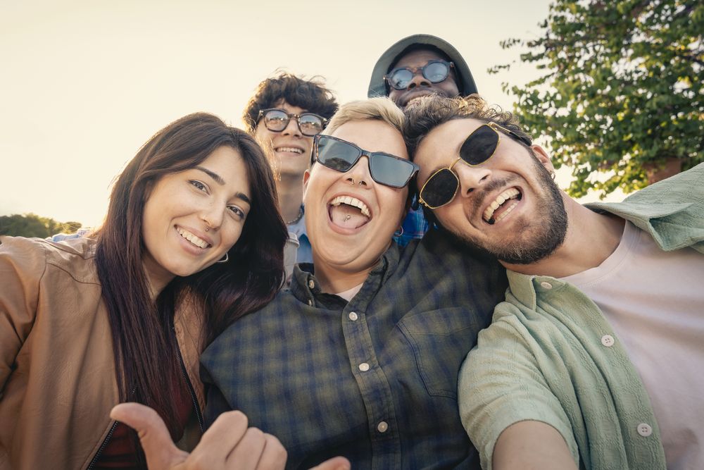 Happy diverse group of young friends taking a fun selfie outdoors at sunset.