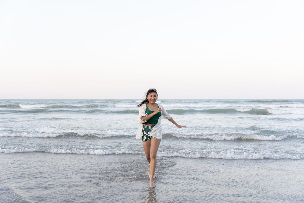 A young Hispanic woman is running from the sea towards the camera at the beach