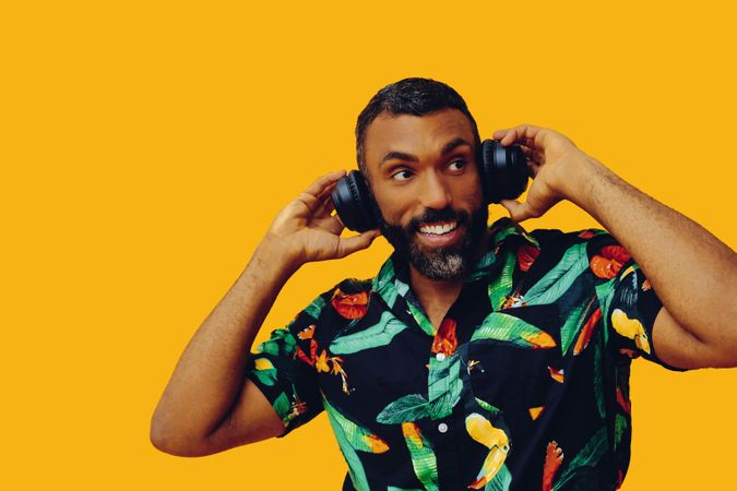 Smiling Black male in bold patterned shirt and headphones in yellow room