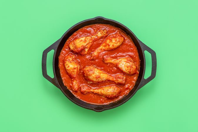 Chicken tomato stew pot, above view on a green background