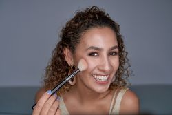 Cheerful woman shading glowing highlighter powder with brush on