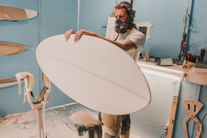 Man holding surf board on stand in workshop