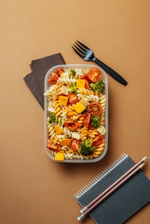 Lunchbox with pasta and plastic fork by notepad and pencils