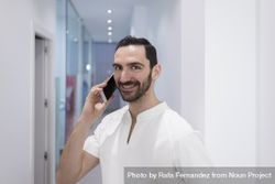 Smiling bearded medical professional talking using a smartphone at hospital 4dOyd5