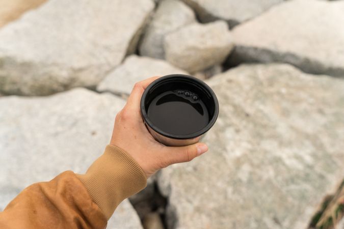 Hand holding coffee atop of rocks