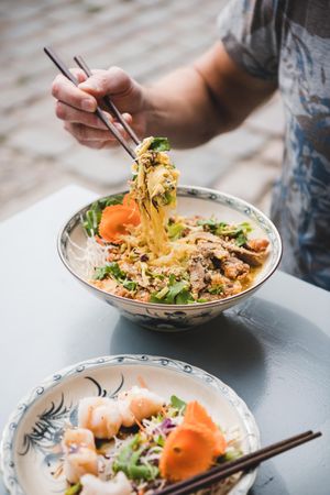 Man eating noodles at Vietnamese restaurant with chopsticks, with appetizer in foreground