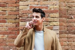 Portrait of confident young man with camel coat walking on cell phone