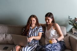 Smiling girlfriends sharing laptop on couch at home
