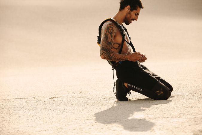 Tattooed man taking a water break after workout on desert sand