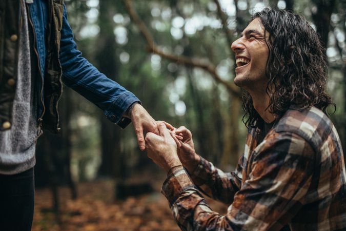 Smiling young man putting engagement ring on woman's hand outdoors under the rain