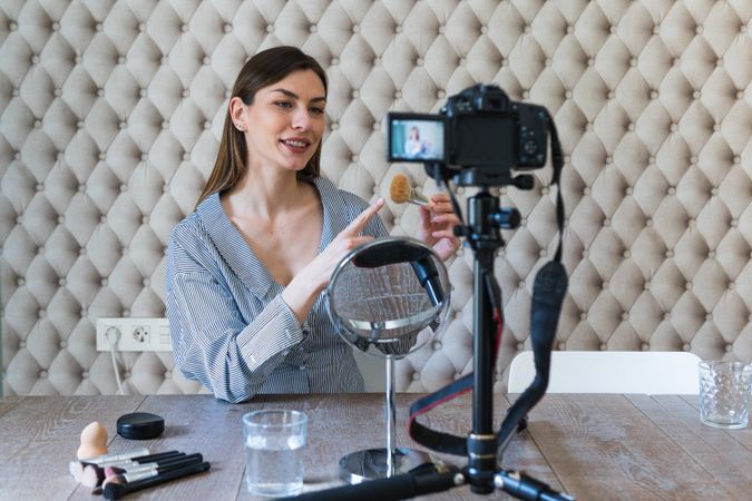 Happy woman applying powder and recording video on camera