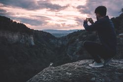 man with photo camera sitting on hill mountain with magnificent sunset