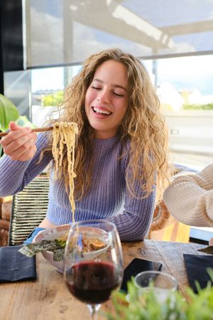 Satisfied fair haired woman eating ramen in restaurant