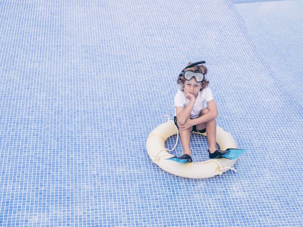 Upset kid with swimming tools on bottom of empty pool