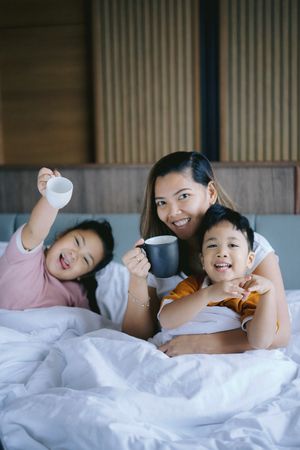 Mother having her morning coffee with children on bed