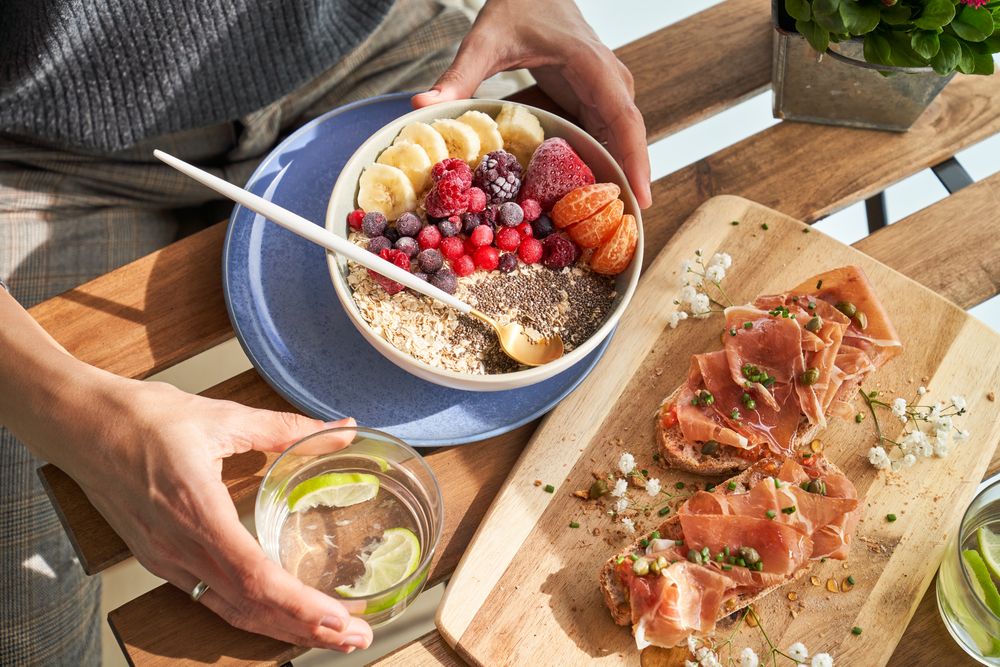 Crop faceless woman sitting at table with assorted healthy food during breakfast