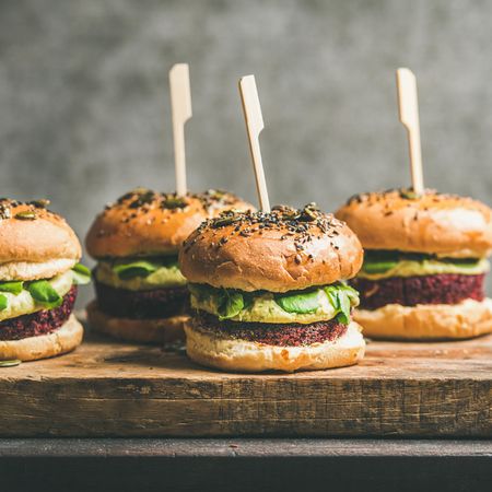 Upright fresh vegan burgers on seeded buns with skewer on wooden board