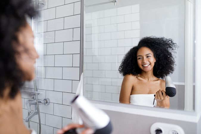 Woman styling her curly hair in a bathroom mirror after a shower