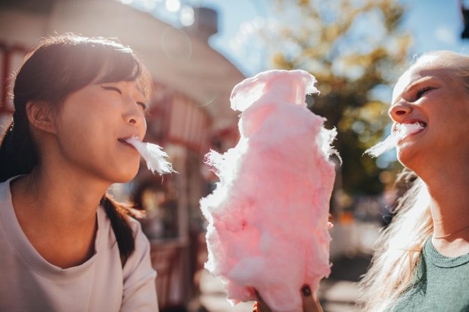 Two young women sharing cotton candy at amusement park