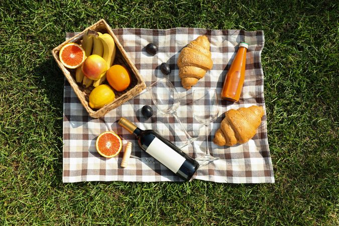 Composition with wine, croissants, fruits and towel on grass, top view