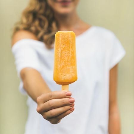 Woman in t-shirt holding orange popsicle, square crop