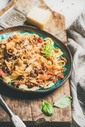 Pasta dinner with minced meat, and cheese on wooden board, vertical composition, selective focus