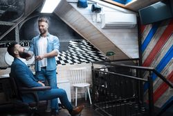 Man in blue suit having his beard trimmed in modern barbershop