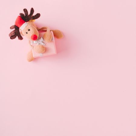 Christmas present with reindeer toy on pink background