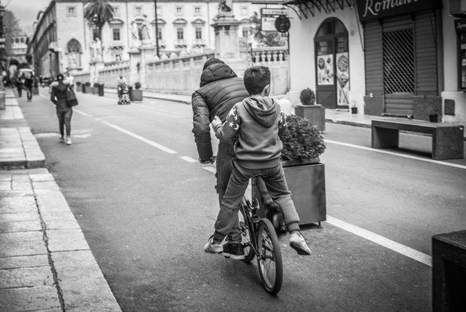 Two boys riding a bicycle on road in grayscale