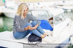 Mature woman using her smartphone sitting in a sea port 4jqy95