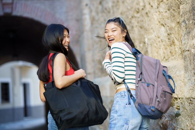 Two women in jeans outside looking back with bags and camera