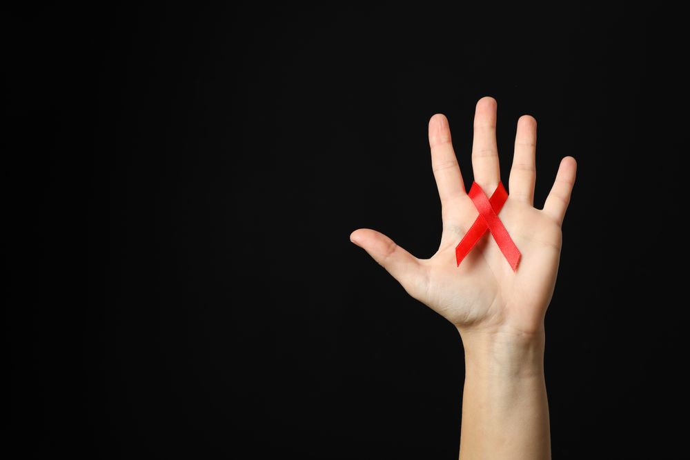 Hand and red awareness ribbon against dark background, space for text