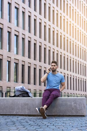 Man in blue t-shirt speaking on phone while sitting outside building