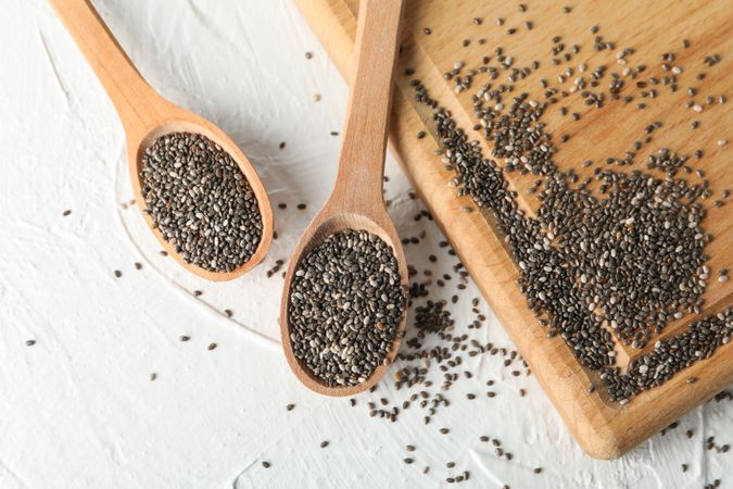 Wooden spoons with chia and board on plain background, space for text
